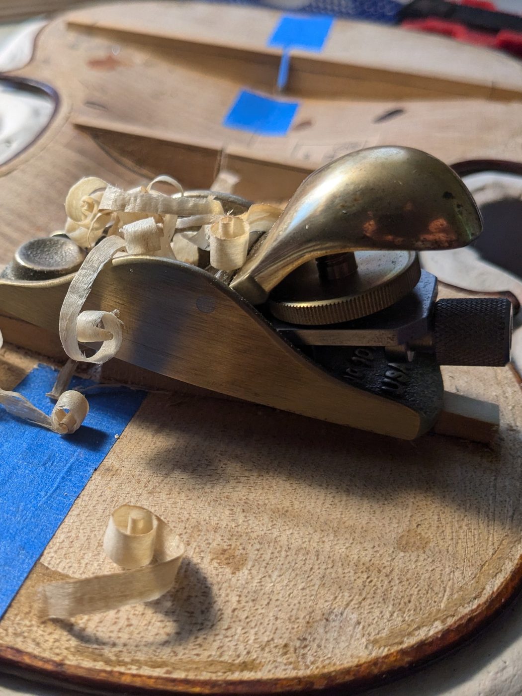 Rabot et copeaux sur un violon en cours de travail à l'atelier, en lumière rasante
